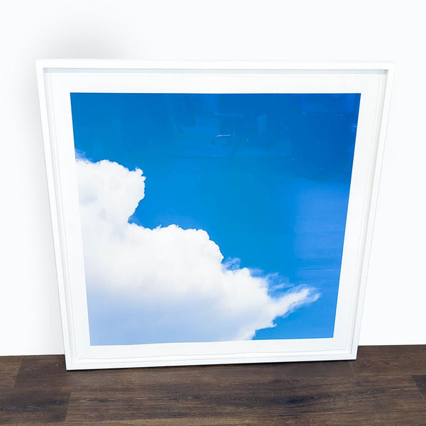 1. Framed Reperch wall print featuring a bright blue sky and white clouds, displayed on a wooden floor.