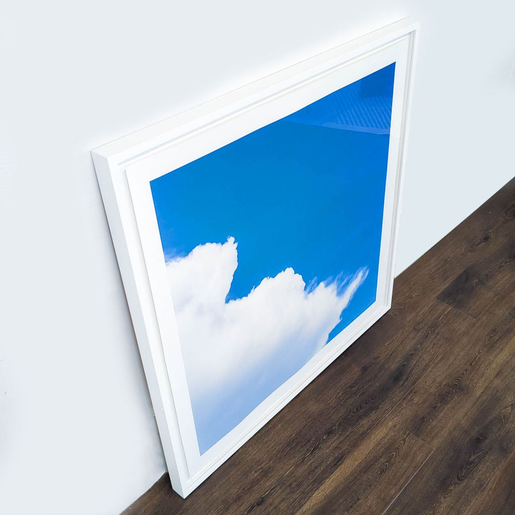 2. Angled view of a Reperch sky print with white frame, showing fluffy clouds against a vivid blue background.