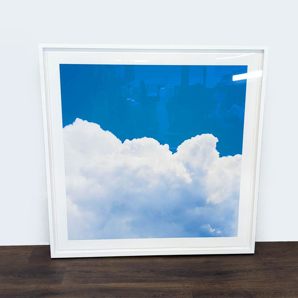 1. Square Reperch print featuring fluffy white clouds against a bright blue sky, framed in white, on the floor.