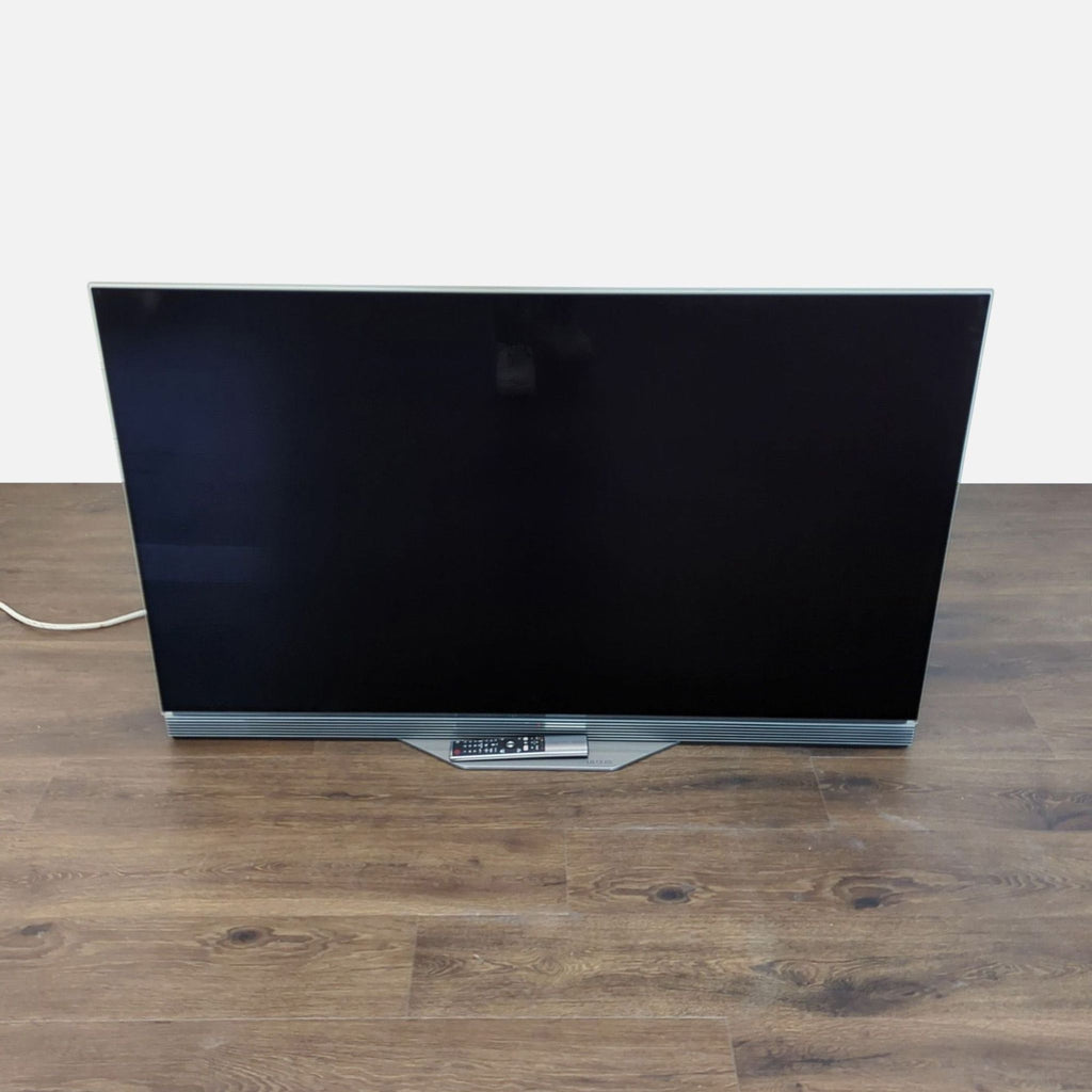1. LG OLED55E7P 55-inch 4K OLED TV with slim glass design and remote, shown powered off on a wood floor.