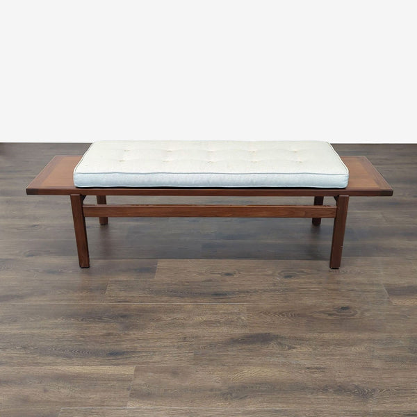 Mid-century modern Reperch bench with wooden frame and white tufted cushion on dark floor.  