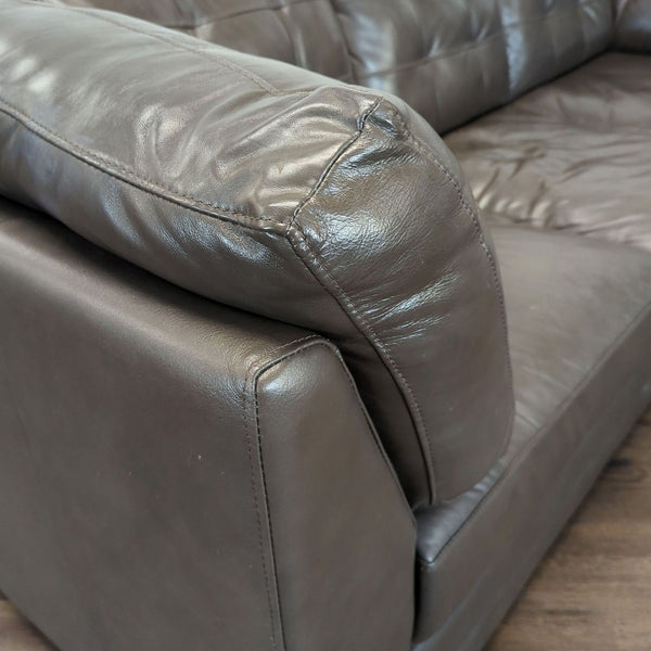 1. Close-up of a Reperch 3-seat sofa arm and cushion in dark brown leather with visible stitching.