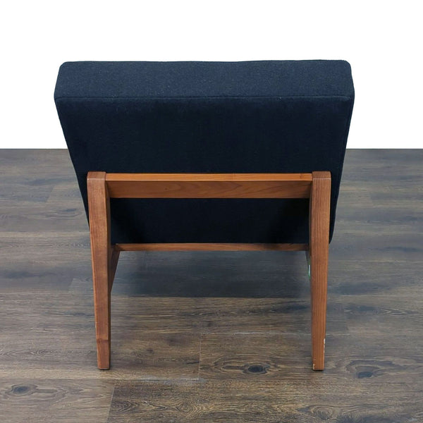 1. Rear view of a Room & Board lounge chair with a black cushion and wooden frame on a wood floor.