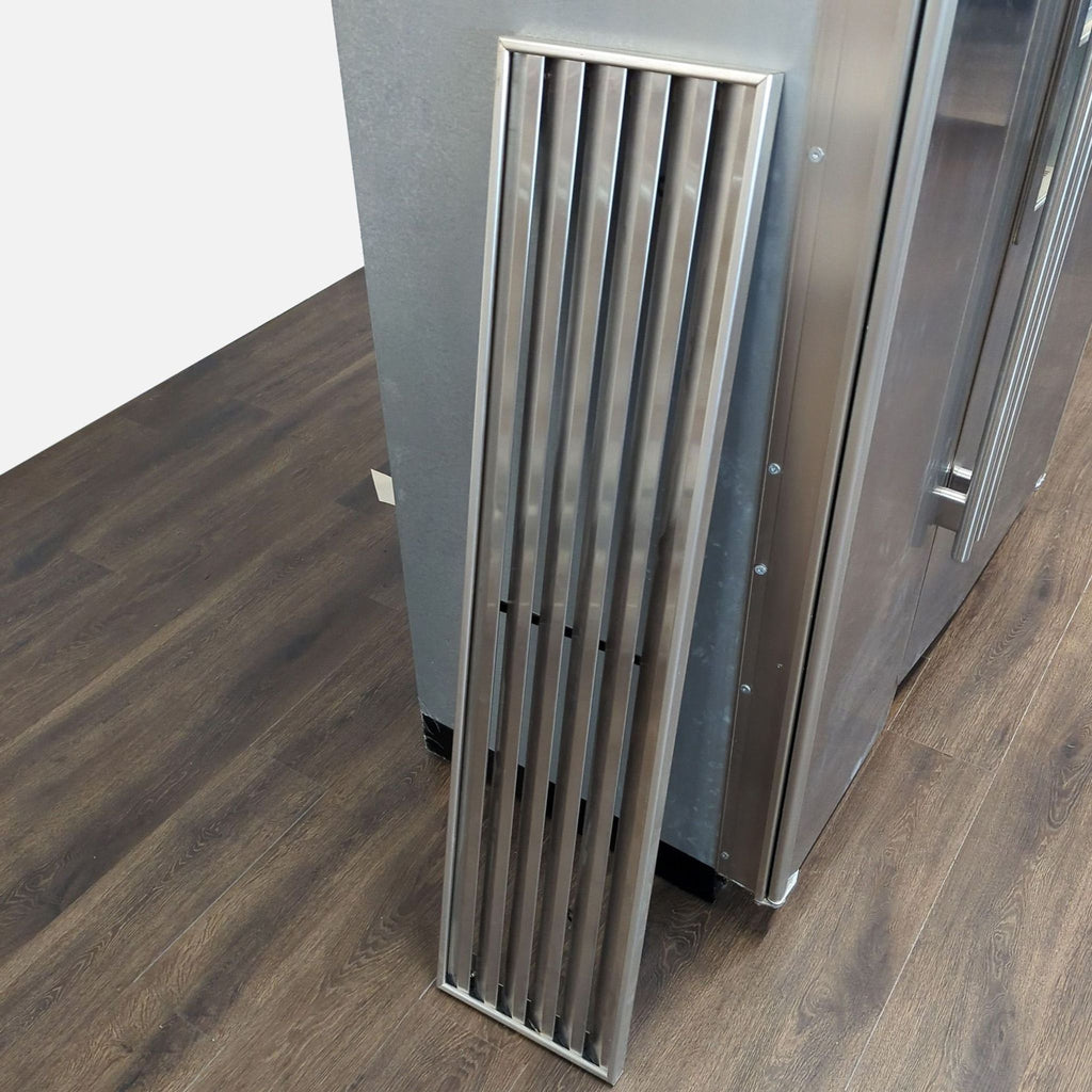 3. Close-up of a detached stainless steel vent panel leaning against the Sub-Zero refrigerator’s side.