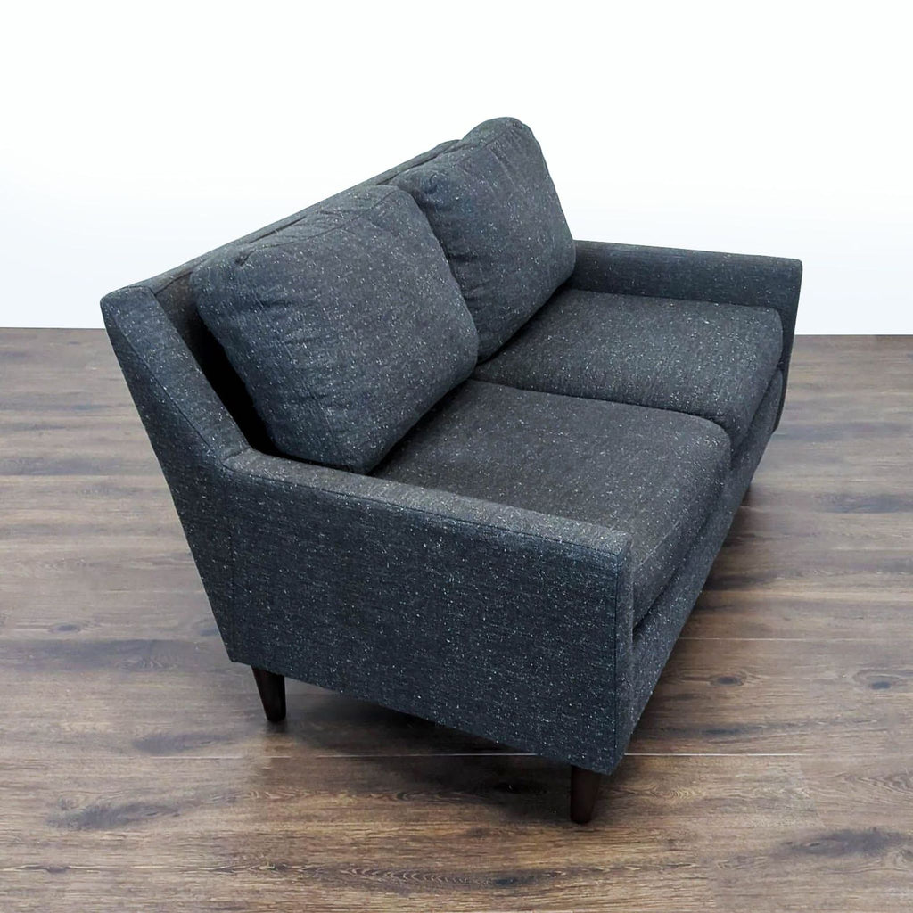 2. Angled view of a West Elm loveseat showing its modern lines and textured dark gray upholstery.  