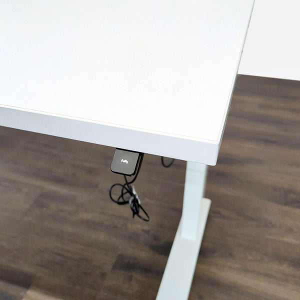 1. Close-up of a white Fully standing desk with electronic control and cable management on a dark wood floor.