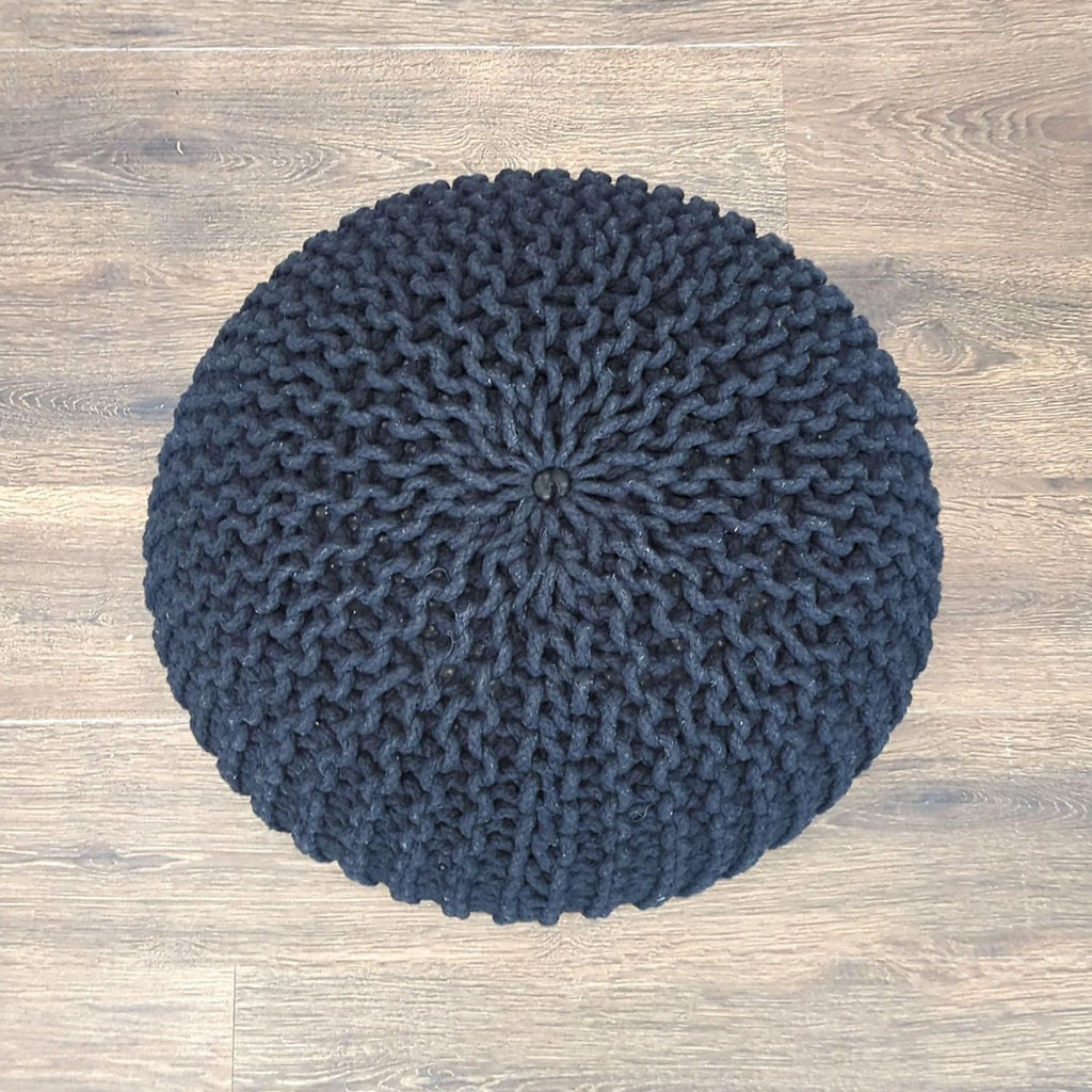 Top view of a circular, black knitted pouf ottoman by Reperch, showing woven details and flat surface.