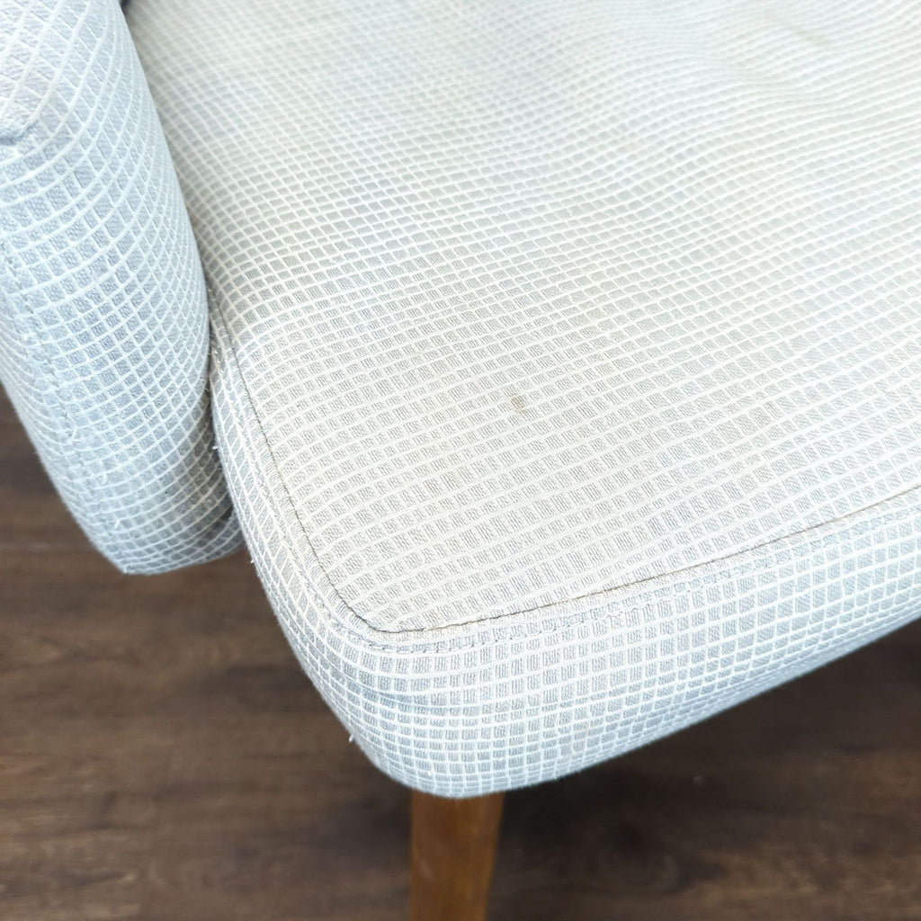 1. Close-up of a West Elm dining chair seat with light patterned upholstery and wooden legs on a wood floor.  