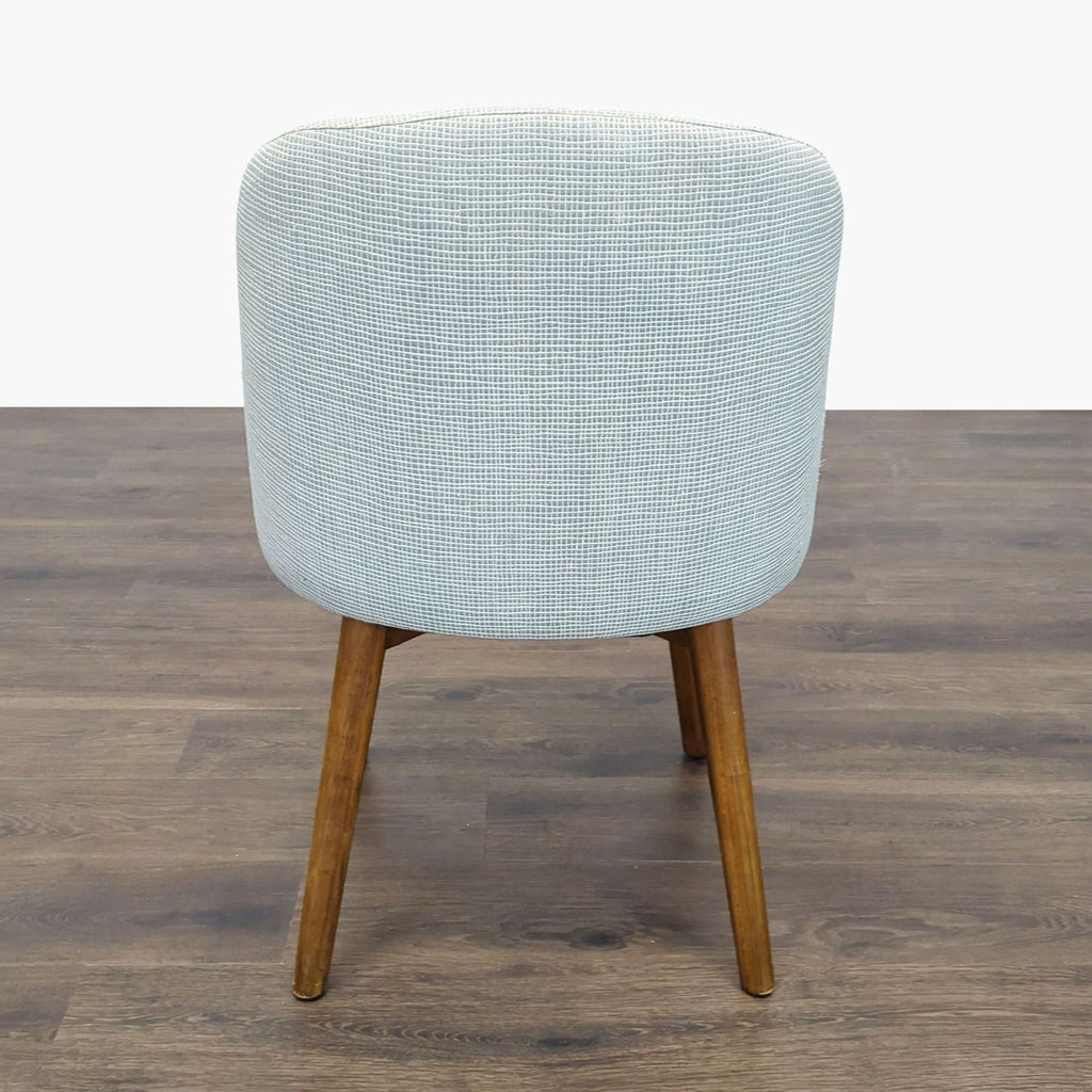 2. Back view of a West Elm dining chair showcasing curved light fabric upholstery and wooden legs on a brown floor.  