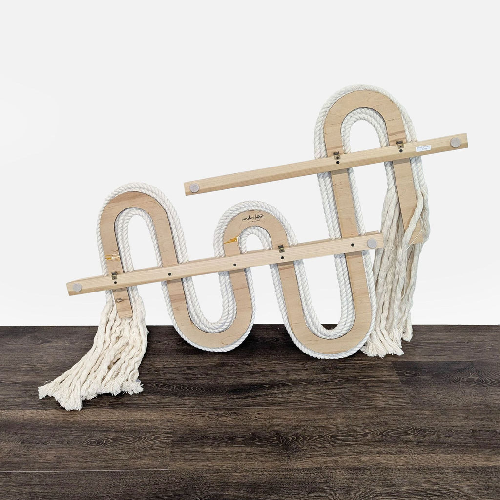 1. Decorative wall art piece by West Elm featuring curved wood and thick white rope with fringe ends on a dark floor.  