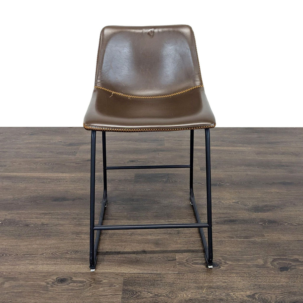 2. Front view of a Reperch brown faux leather stool with black metal legs on a wood floor.