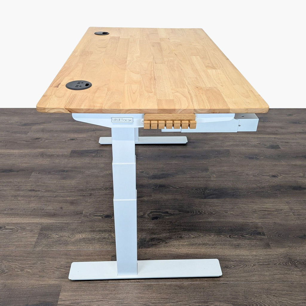 2. Side view of Uplift adjustable desk with light wood surface, white legs, cable ports, and a wooden accessory rack.  
