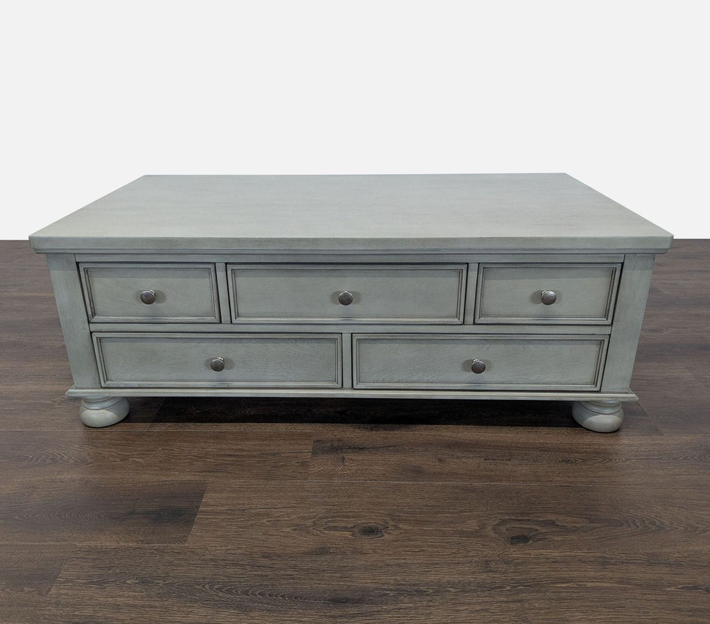 1. Reperch Coffee Table in gray finish, features five drawers and round feet, shown on wooden flooring.