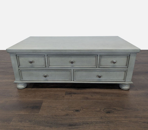 1. Reperch Coffee Table in gray finish, features five drawers and round feet, shown on wooden flooring.