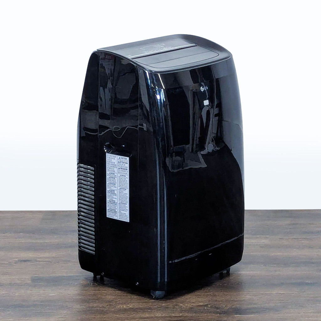 2. Angled side view of a compact LG portable air conditioner in black, featuring wheels and simple design.