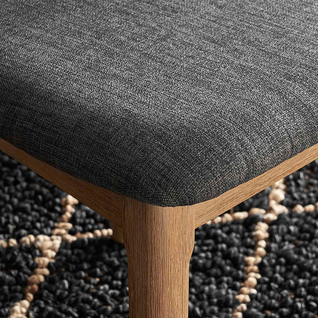 Close-up of Reperch dining chair, highlighting padded grey performance fabric seat and acacia wood detail.