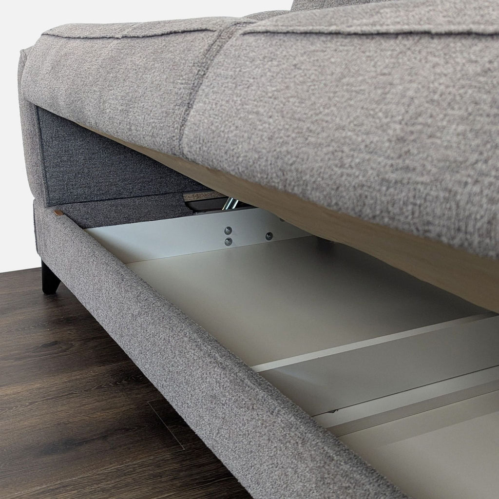 2. Close-up of the built-in storage compartment under the seat of the grey Reperch 3-seat sofa.