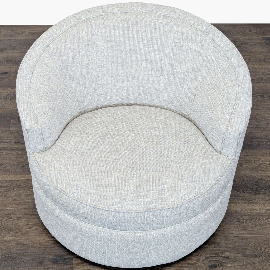 1. Top view of a round, light gray lounge chair by Reperch with soft fabric and curved backrest on wood floor.  