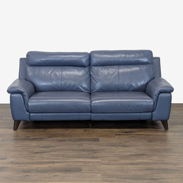 Front view of a modern blue leather Living Spaces sofa with wide armrests and wooden legs on a wood floor.