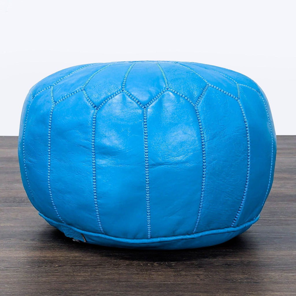 Bright blue leather ottoman by Reperch with detailed stitched panels, shown on a dark wooden floor.