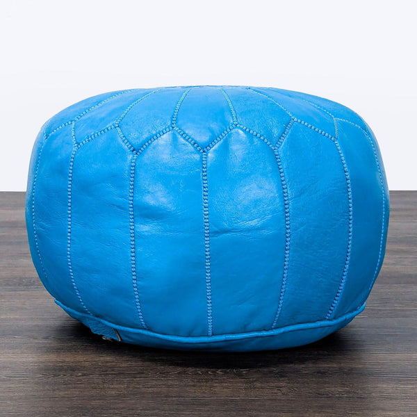 Bright blue leather ottoman by Reperch, featuring stitched geometric panels, on a wooden floor.  