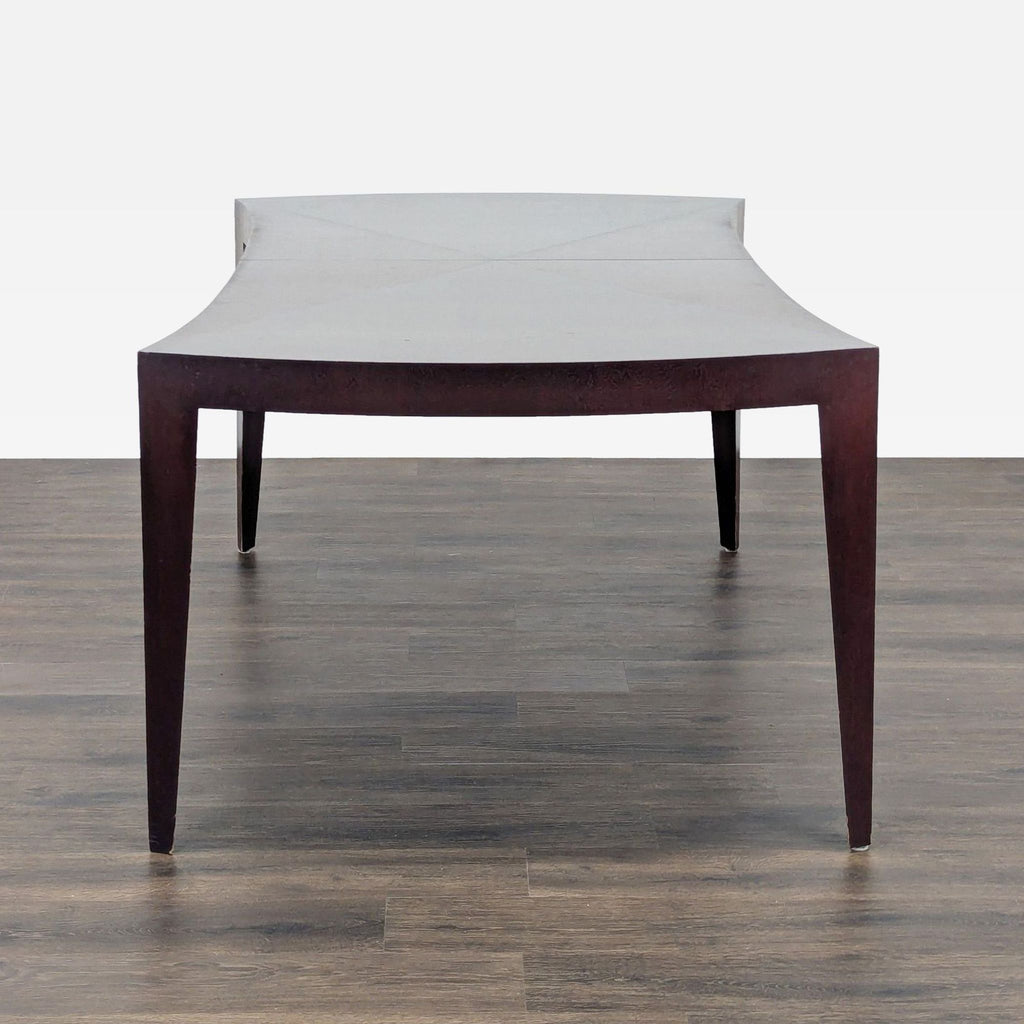 3. Side view of a New Studio dining table featuring a contemporary dark wood frame and curved design.