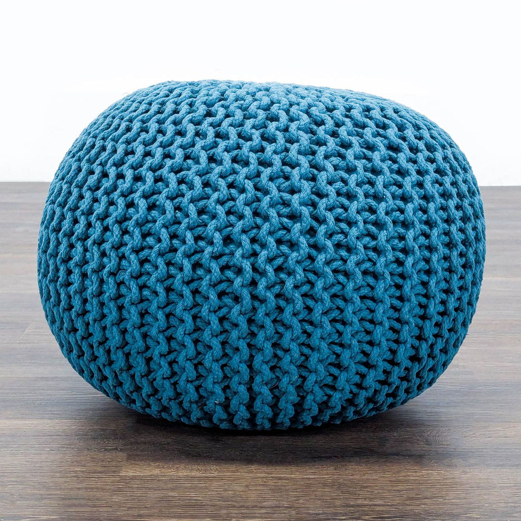 1. Close-up side view of a round blue knitted pouf ottoman by Reperch on a wooden floor.