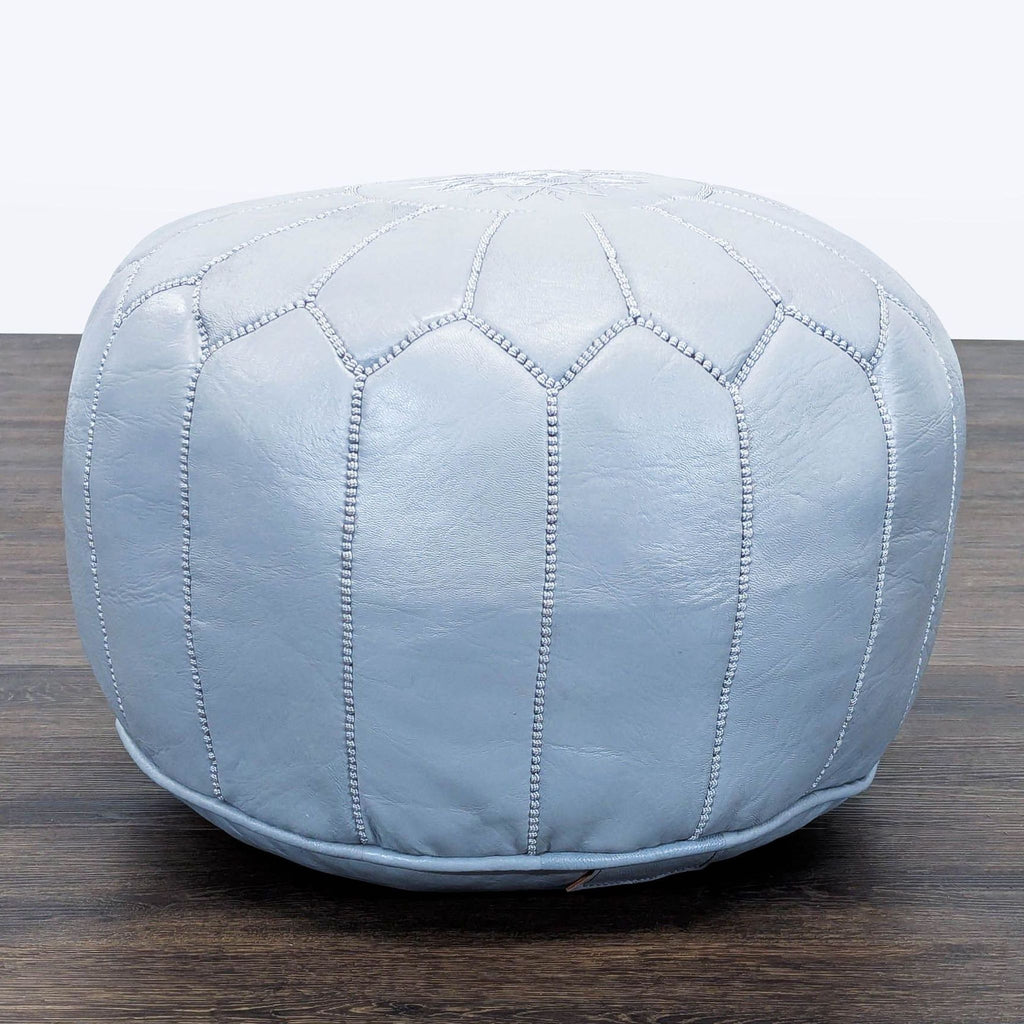 1. Light blue Reperch ottoman with decorative stitching, round shape, on a dark wood floor.