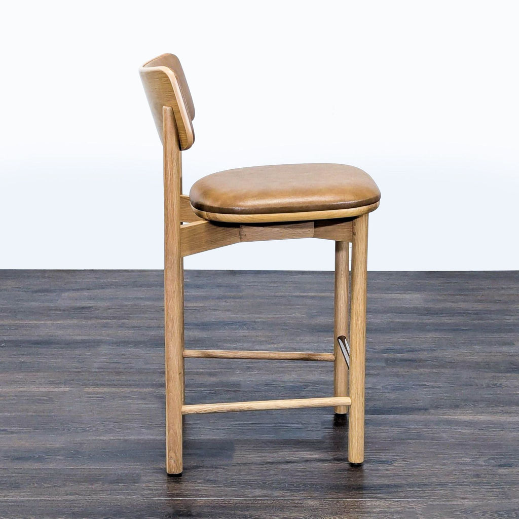 3. Side profile of West Elm stool, showing oak legs, curved vinyl-upholstered seat, and engineered wood backrest.