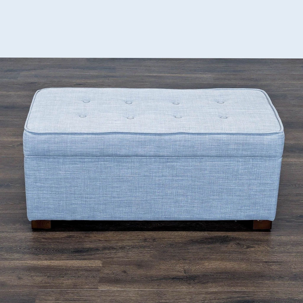 1. Light blue rectangular ottoman from Target, featuring button-tufted top and short wooden legs on a wood floor.