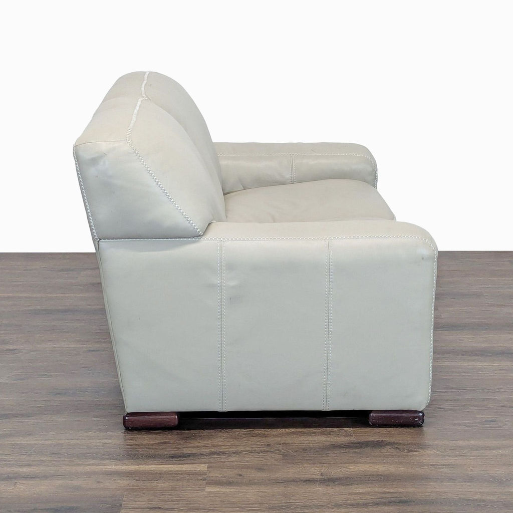 2. Side view of a modern Reperch loveseat in cream leather, displaying broad armrests and plush cushions.