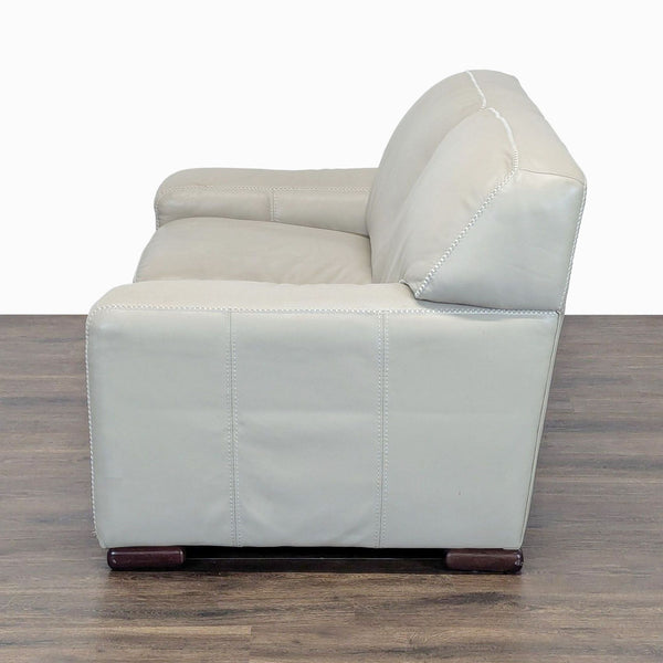 Side view of a Reperch loveseat in light leather, showing plush cushions and wooden legs on a wood floor.  