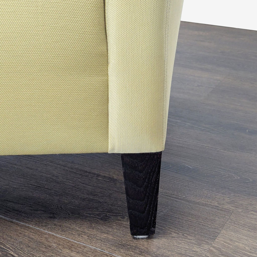 Close-up of the textured fabric upholstery and sturdy dark leg of a Reperch lounge chair on wooden flooring.