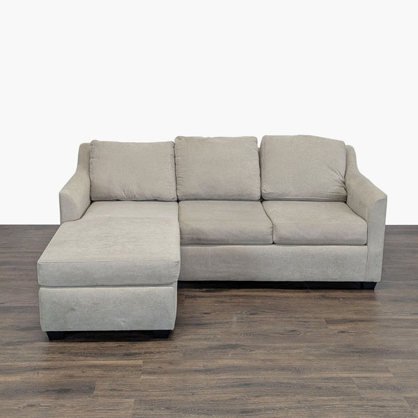 Modern beige Living Spaces 3-seat sectional sofa with chaise, shown from the front on wood flooring.