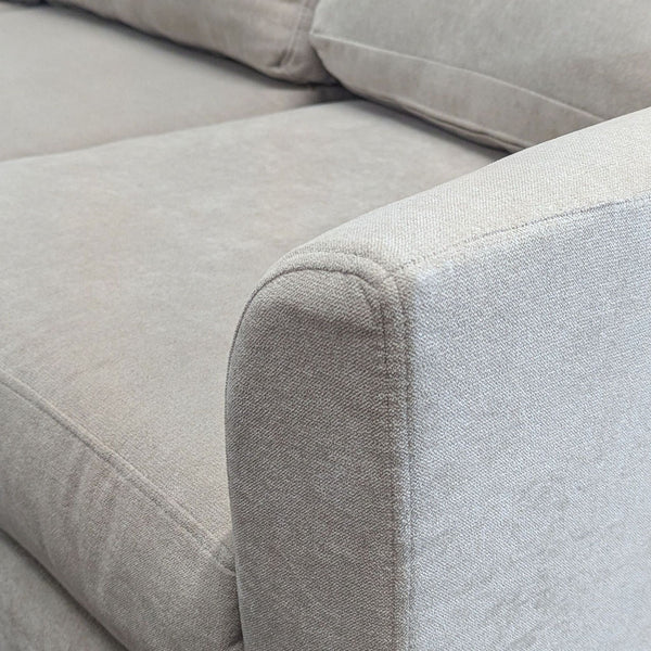 Close-up of a Living Spaces 3-seat sofa armrest featuring light beige upholstery and plush cushions.  