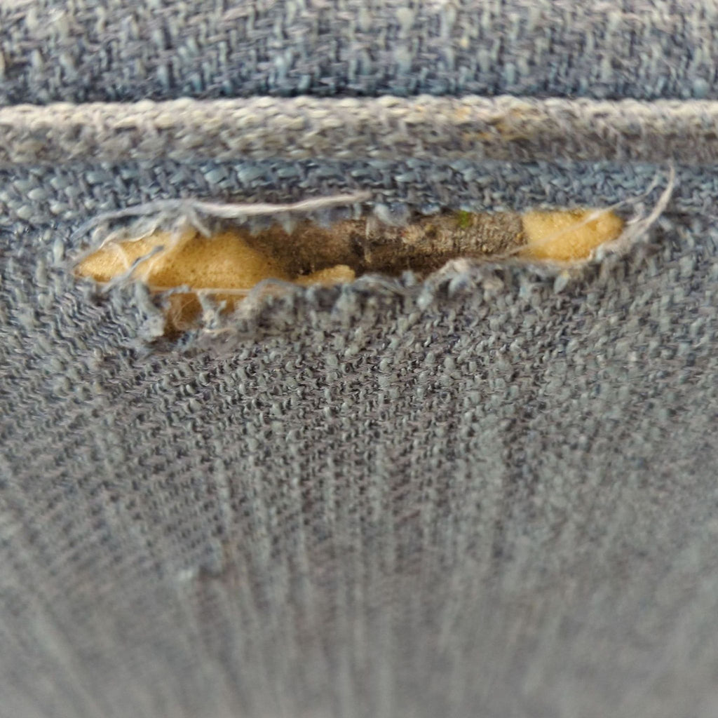 3. Detailed close-up of a tear in the blue fabric upholstery, exposing yellow foam inside the Noble House Home stool.