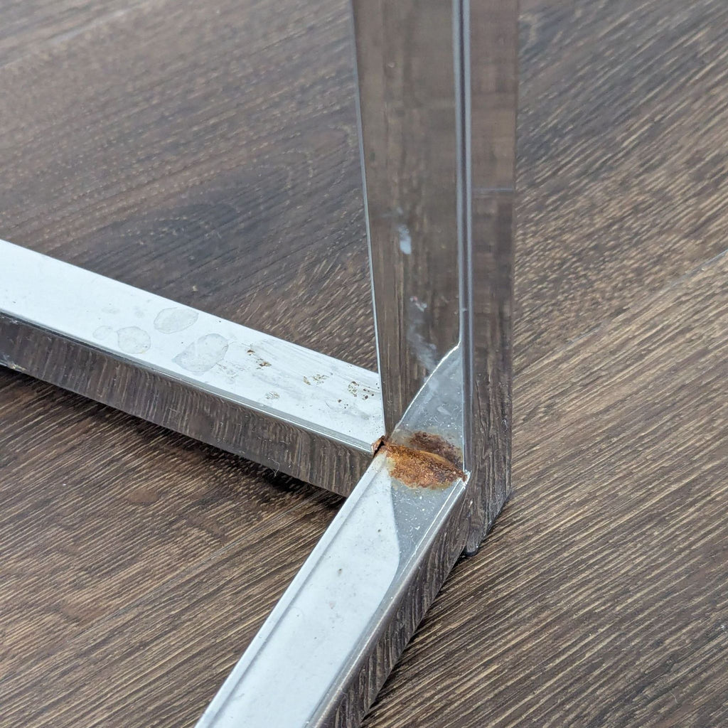2. Bottom corner of a Reperch end table frame, showing chrome metal with visible rust and smudges.  