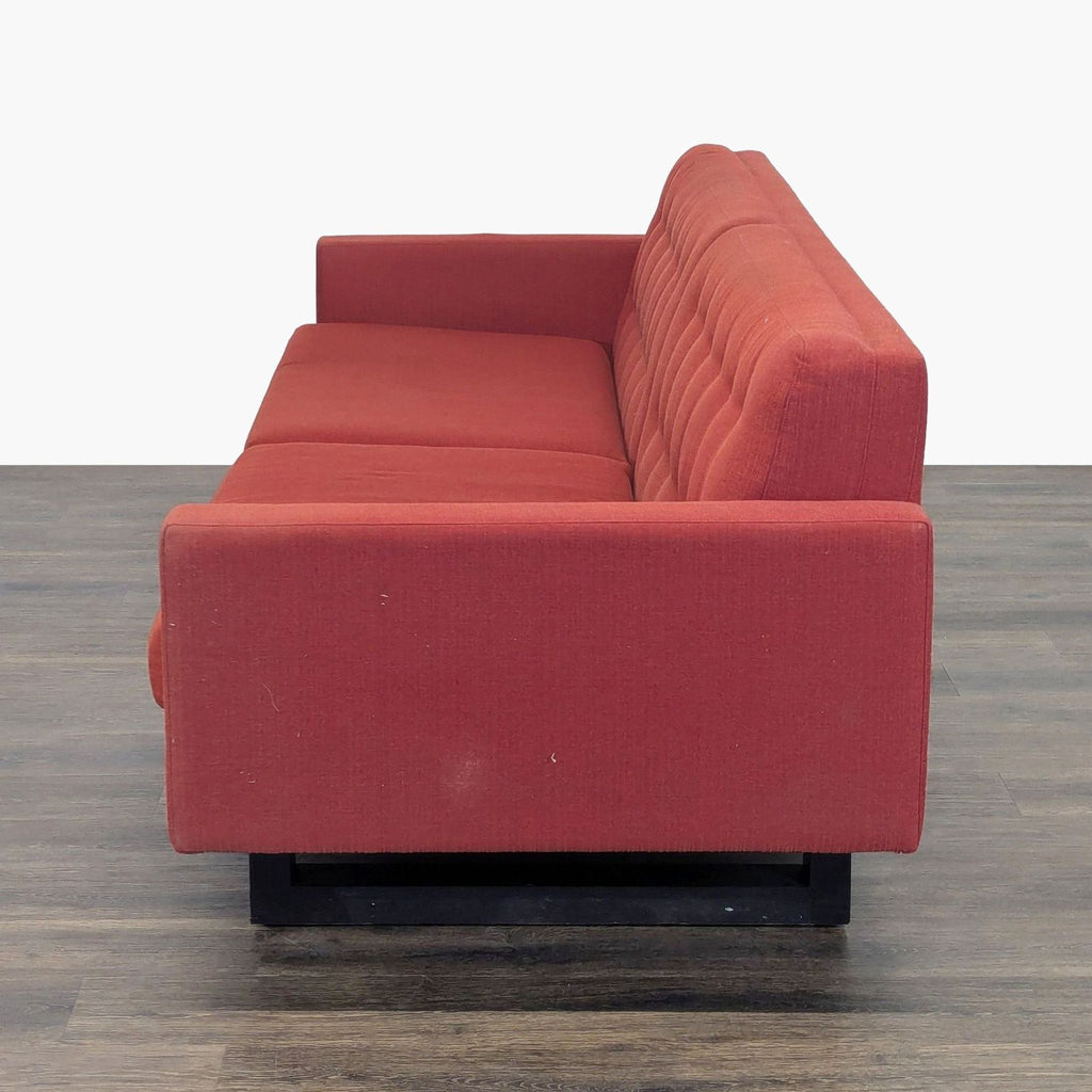 Side view of a red Room and Board 3-seat sofa with square arms and a tufted backrest on wood flooring.  