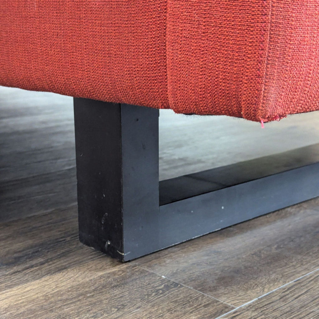 Detail of the black metal leg and lower edge of the red Room and Board 3-seat sofa on wood flooring.