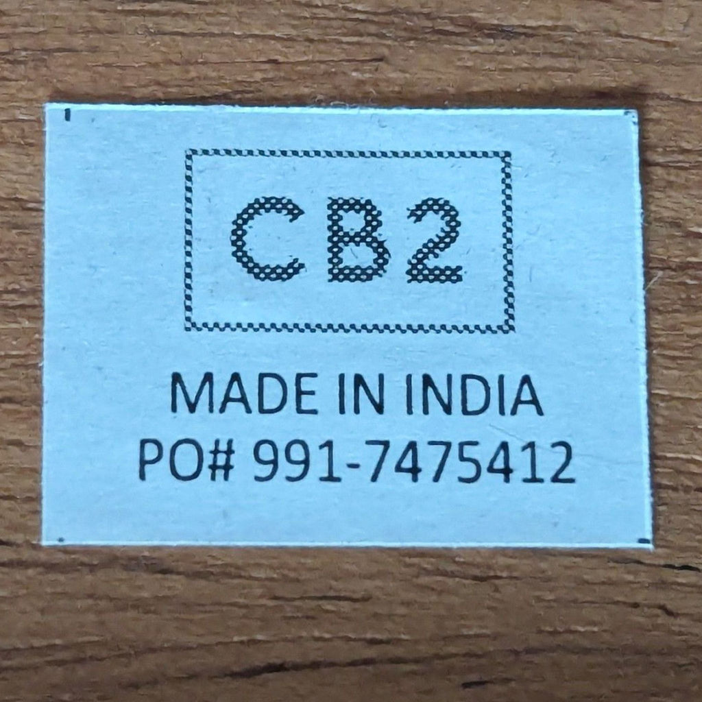 2. Label reading "CB2 Made in India PO# 991-7475412" on wood, indicating brand and origin of the entertainment center.