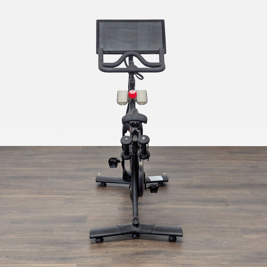 1. Front view of a Peloton stationary bike with a large screen, set on a wooden floor.