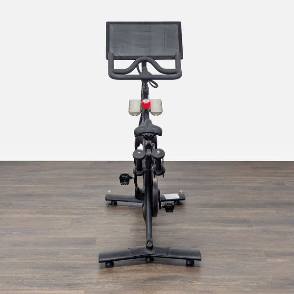 1. Front view of a Peloton stationary bike with a large screen, set on a wooden floor.