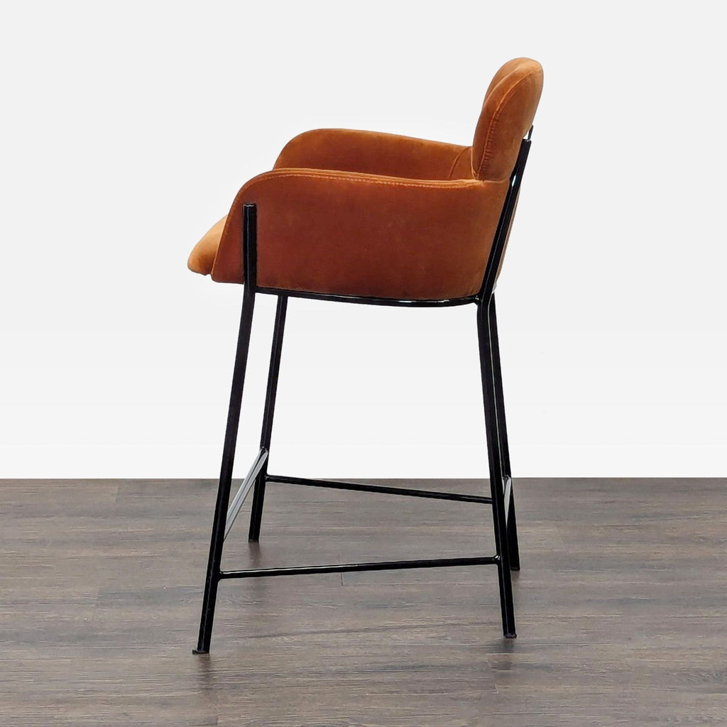 3. Side profile of a CB2 stool with plush velvet seat, curved armrests, and sleek black metal legs.