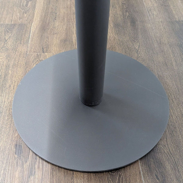 1. Close-up of a Ventana side table's round black metal base on a wood floor.  