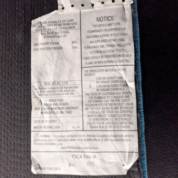 1. Close-up of a Room & Board frame tag listing materials, safety, and manufacturing details in black text.