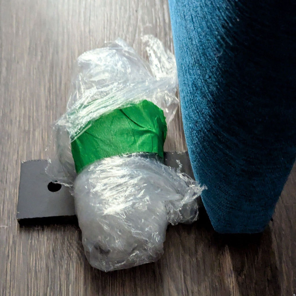 2. Furniture frame leg from Room & Board wrapped in plastic and green tape on a wood floor next to blue upholstery.