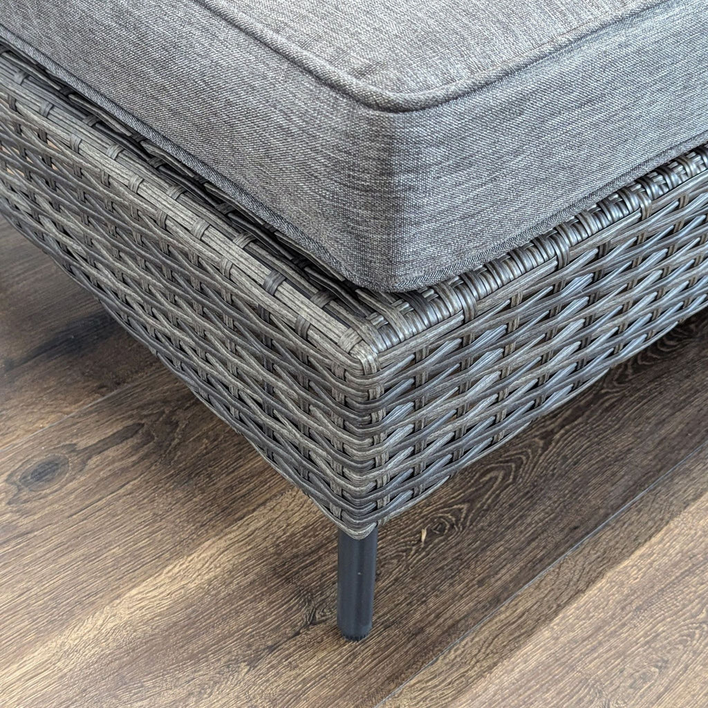 3. Detailed image of the woven rattan texture and metal leg of a Reperch set’s ottoman with gray cushion.