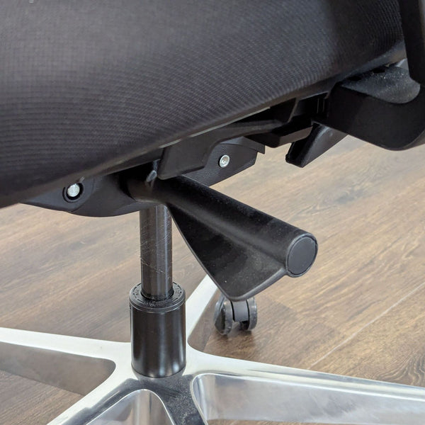 1. Close-up of the adjustment lever and base of a Branch office chair on a wood floor.