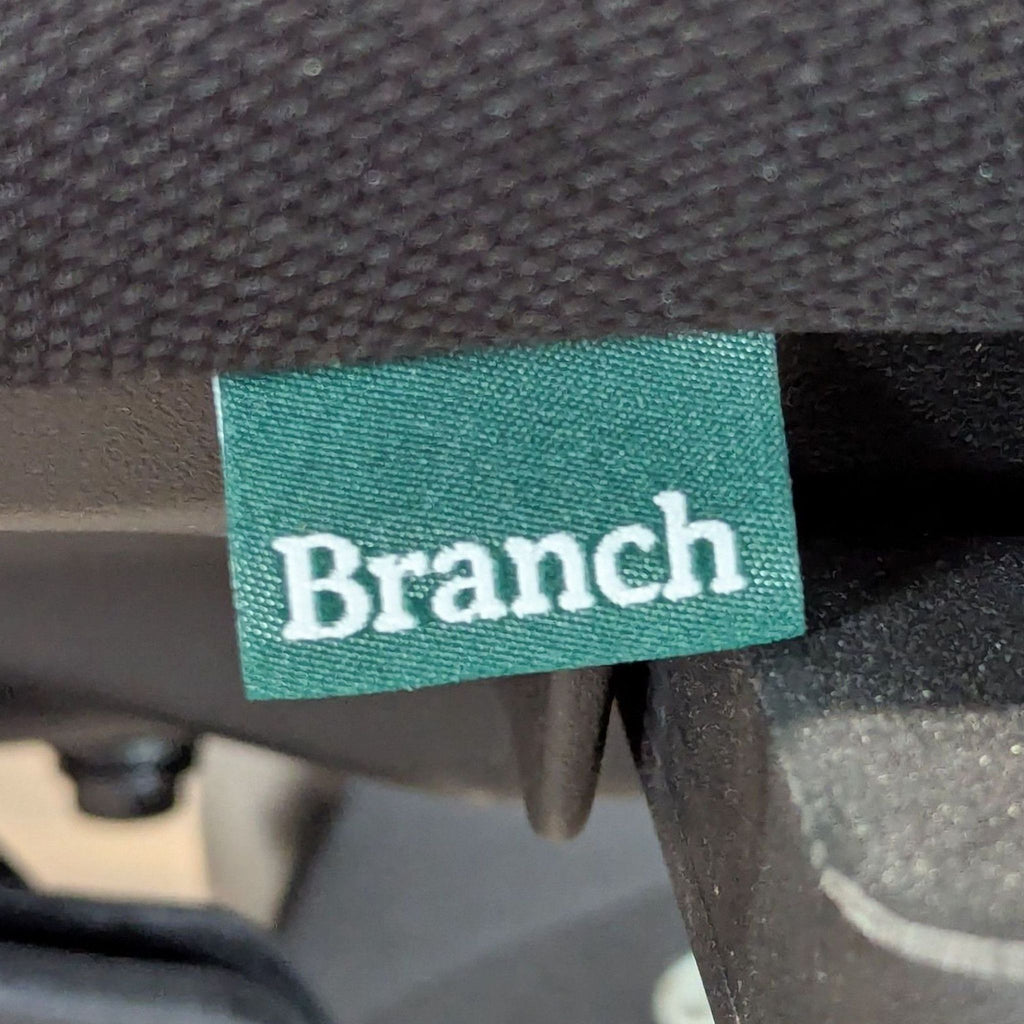 2. Green fabric tag with the white Branch logo attached to a black mesh office chair.
