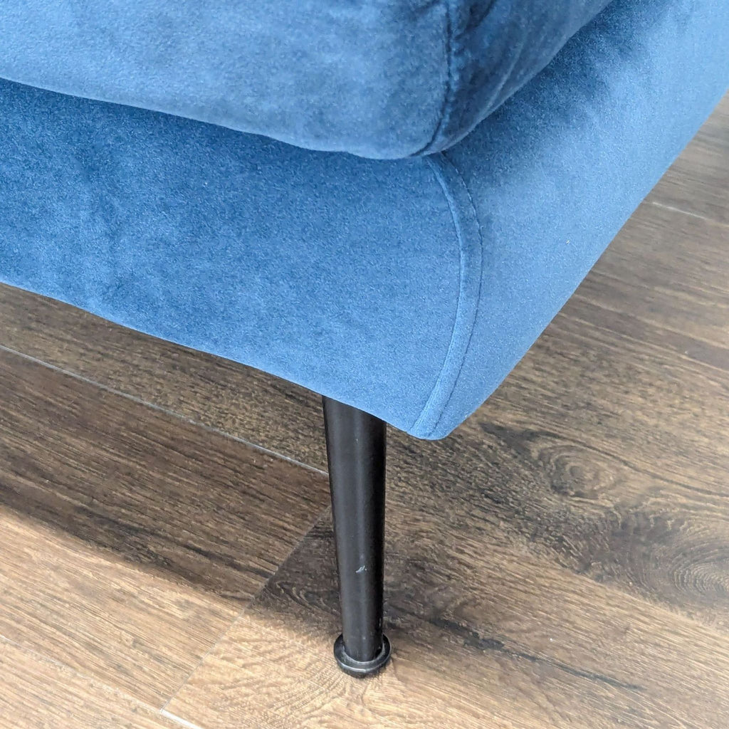 Detail of the blue Edloe Finch lounge sofa base and black metal leg on a wood floor background.